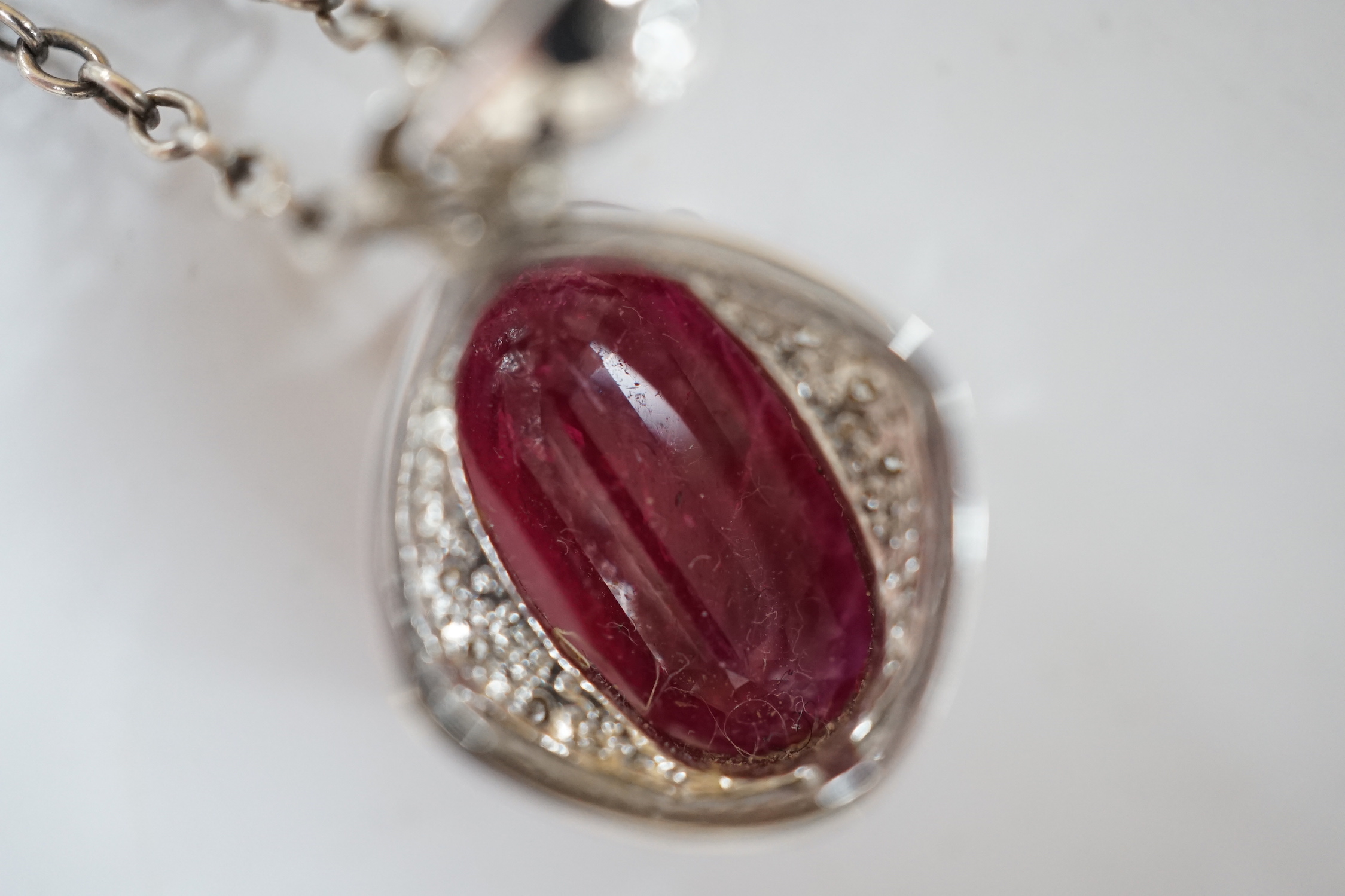 A modern 18ct white gold, ruby and diamond set oval cluster pendant, 24mm, on a white metal chain.